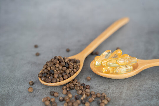 Black pepper granules in wooden spoon with black pepper capsules The piperine found in black pepper has anti-obesity properties. and burn fat well.