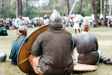 Resting warrior barbarian in armor, helmet and with a sword outdoors, back view. Medieval festival...