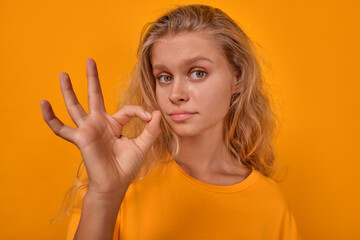 Young confident cute Caucasian woman shows OK gesture to confirm agreement to go on date or give...