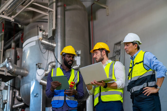 Group Of Diversity Electrical Engineer In Safety Uniform Working Together At Factory Site Control Room. Industrial Technician Worker Maintenance And Checking Power System At Manufacturing Plant Room.