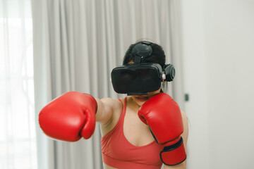 Embracing the future of fitness, an Asian woman dons VR glasses and boxing gloves for an invigorating home exercise.