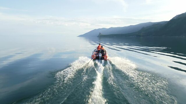 The motor boat is moving at speed on Lake Baikal against the backdrop of beautiful landscapes of rocks. The view from the drone. The sky is reflected in the surface of the water