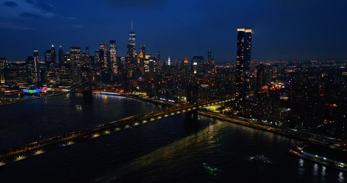 Vibrant New York cityscape full of lights. View of midtown and bridges from drone flying above the East River.