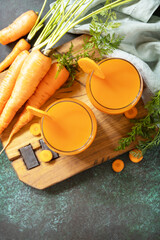 Carrot juice in a glass and fresh carrots with leaves on a stone table. Carrot healthy juice for detox. Healthy vegan vegetarian drink. View from above. Copy space.