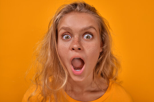Total sale and huge discount concept. Close up portrait of wow stunned blonde freckles Caucasian woman with big eyes and wide open mouth screams, standing on yellow background.