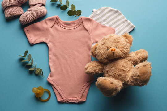 Flat lay of pink baby grow, hat, teddy bear and pink booties with copy space on blue background