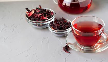 Herbal tea made from hibiscus petals in a transparent cup on a light background, teapot and a bowl of dry hibiscus.