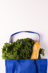 Blue canvas bag with baguette and green salad vegetables and copy space on white background