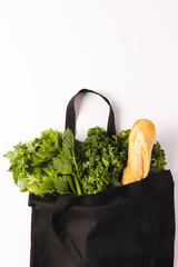 Black canvas bag with baguette and green salad vegetables and copy space on white background