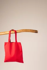 Foto op Plexiglas Red canvas bag hanging from wooden branch with copy space on white background © vectorfusionart