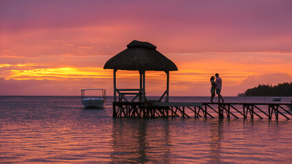 Man and Woman watching sunset on a wooden pier in the ocean on a tropical beach in Mauritius, a couple on a honeymoon vacation in Mauritius