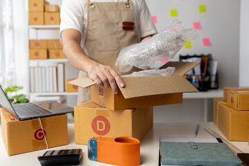Male owner of an online store packs products into parcel boxes based on orders from online sales sites, packs products for delivery to addresses via private courier service. Product packaging concept.