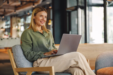 Stylish woman freelancer working on laptop in cozy coworking and looking at side