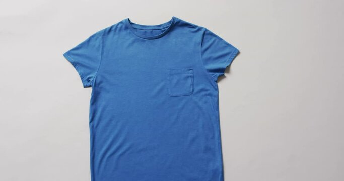 Video of flat lay of blue t shirt with copy space on white background
