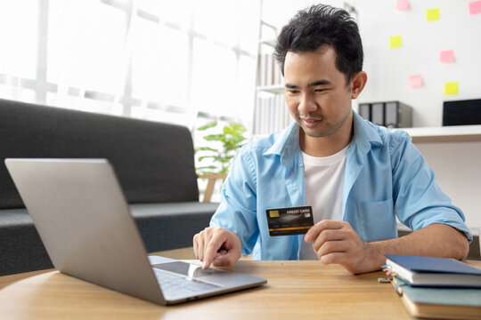 Asian man holding a credit card, he is filling in credit to pay for goods and services on the internet, using credit card to pay for services. Credit card spending concept.