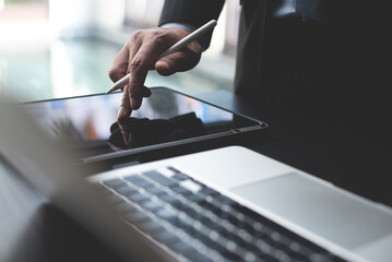 Obraz premium Closeup of businessman hand using digital tablet and working on laptop computer. Business man planning work project, searching the information, surfing the internet on office table
