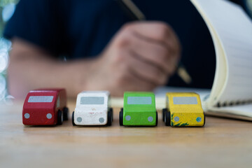 Many wood car with blur background of a man writing on notepad or book. Finance of the car is calculating the cost of reserving car. Transportation rental automotive business concept