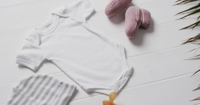 Video of white baby grow, hat, dummy and pink booties with copy space on white background