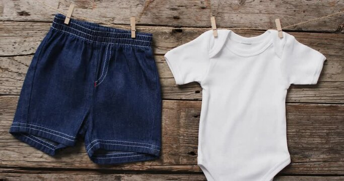 Video of baby grow and denim shorts hanging on clothes pegs with copy space on wooden background