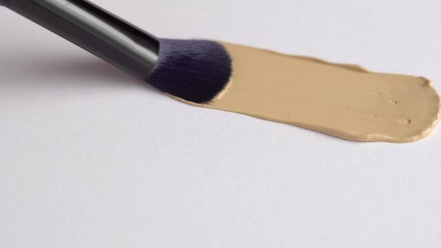 A smear of foundation cream or concealer with a brush on a white background, macro. Texture of cosmetic liquid foundation or beige cream smudge, smear, stroke. Advertising of professional cosmetics.