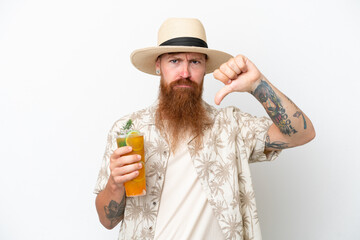 Redhead man with long beard drinking a cocktail on a beach isolated on white background showing thumb down with negative expression