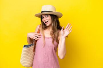 Young caucasian woman holding a beach bag isolated on yellow background saluting with hand with happy expression