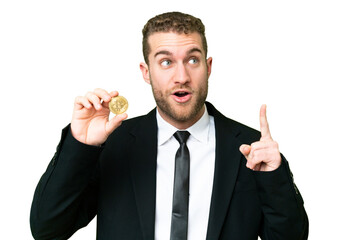 Young business blonde man holding a Bitcoin over isolated chroma key background thinking an idea pointing the finger up