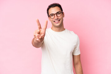 Young caucasian man isolated on pink background smiling and showing victory sign