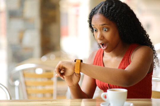 Amazed black woman checking smartwatch in a bar