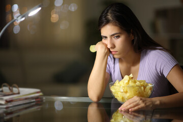 Sad woman eating portato chips complaining in the night