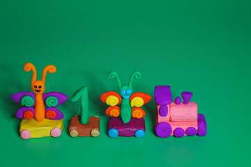 Toy train made of plasticine with butterflies and the number 1. Birthday. A festive event. Green background.