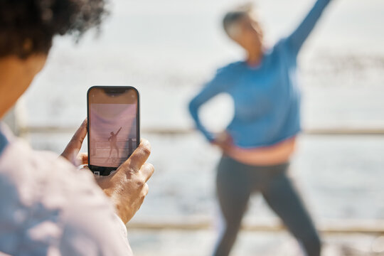 Phone, fitness and photograph of woman at beach in silly pose at sea for senior friends. Exercise, mobile and picture for social media post on a ocean promenade walk for nature workout and friendship
