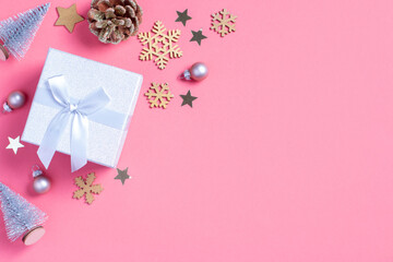 Christmas background with golden gift box with mini Christmas trees and baubles on pastel pink background