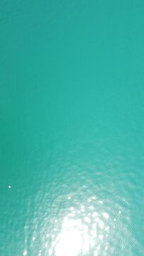 Vertical aerial view on sea water surface, camera flies over clear sea water. Sun glare. Abstract nautical summer ocean nature. Holiday, vacation and travel concept. Nobody. Vertical video
