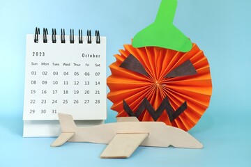 Selective focus of October 2023 desk calendar  with jack o lantern pumpkin decoration and airplane. Halloween travel concept.