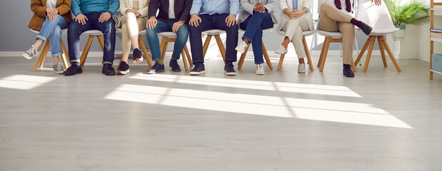 Multiracial group of people sitting in the office. Diverse team of corporate employees wearing smart casual outfits sitting on a row of chairs at work. Cropped shot, human legs, low section