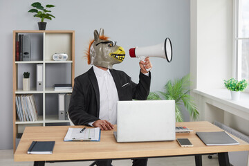 Portrait of funny business man wearing donkey mask sitting at the desk in office and shouting in...