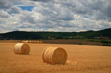 Hay bail harvesting in golden field landscape. Summer Farm Scenery with Haystack on the Background of Beautiful Sunset.