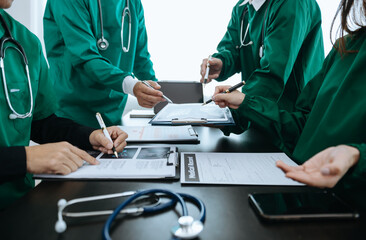 Medical team having a meeting with doctors in white lab coats and surgical scrubs seated at a table discussing a patients working online using computers in the medical industry.