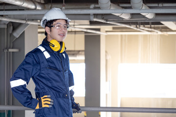 Portrait of Asian confident man construction worker or male maintenance engineer with protective suit, earmuffs, safety helmet and goggles looking away while standing at construction site