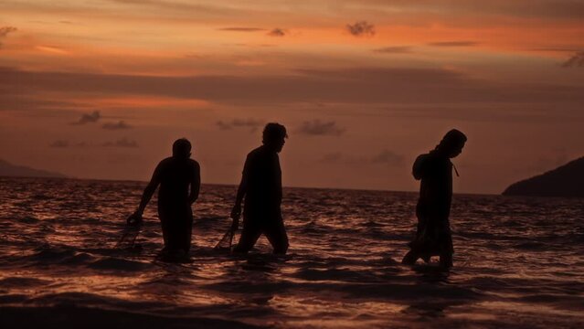 Silhouette of fishermen walking through a shallow sea water in Langkawi, Malaysia at sunset