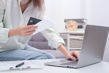 Close up woman holding receipt, using laptop, calculating bills, money, sitting on sofa at home in livingroom, female planning budget, managing expenses, finances, checking internet banking service.
