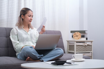 Close up woman holding receipt, using laptop, calculating bills, money, sitting on sofa at home in livingroom, female planning budget, managing expenses, finances, checking internet banking service.
