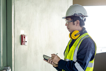 Building inspector man using digital tablet checking wall mounted fire alarm station near fire exit...