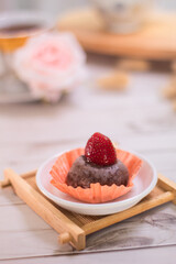 Close up of Japanese dessert chocolate mochi or glutinous rice ball with strawberry topped. served on white plate, cup of tea and rattan coaster. blurred background. aesthetic food