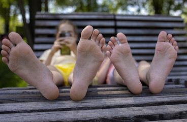 Two girls-sisters of school age relax on a park bench during a walk. View of the feet.