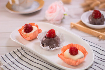 Japanese dessert chocolate and strawberry mochi or glutinous rice ball with strawberry topped. served on white plate and cup of tea. blurred background