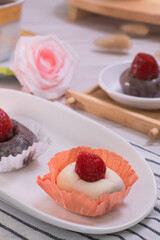 Close up of Japanese dessert chocolate and strawberry mochi or glutinous rice ball with strawberry topped. served on white plate and cup of tea. blurred background