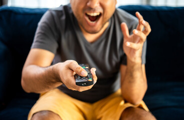 Fototapeta premium Young man watching television with various action. Man holding TV remote changing program menu enjoy watching.