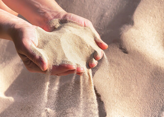 Handful of sand in the women's hands, selective focus. The sand pouring from female hands.	
